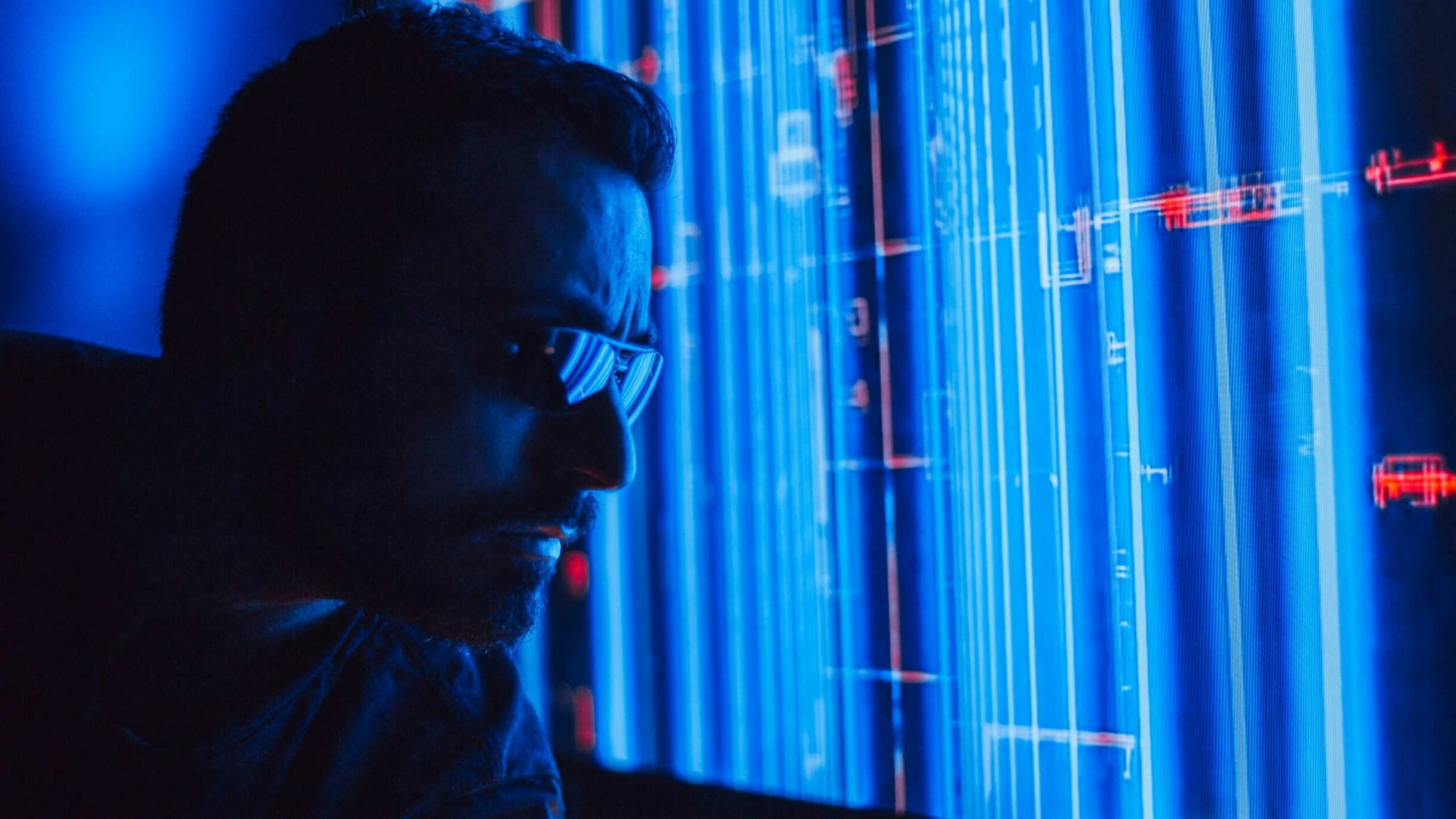 Nos Expertises A man in sunglasses intently studies a vibrant blue holographic screen, symbolizing digital technology.