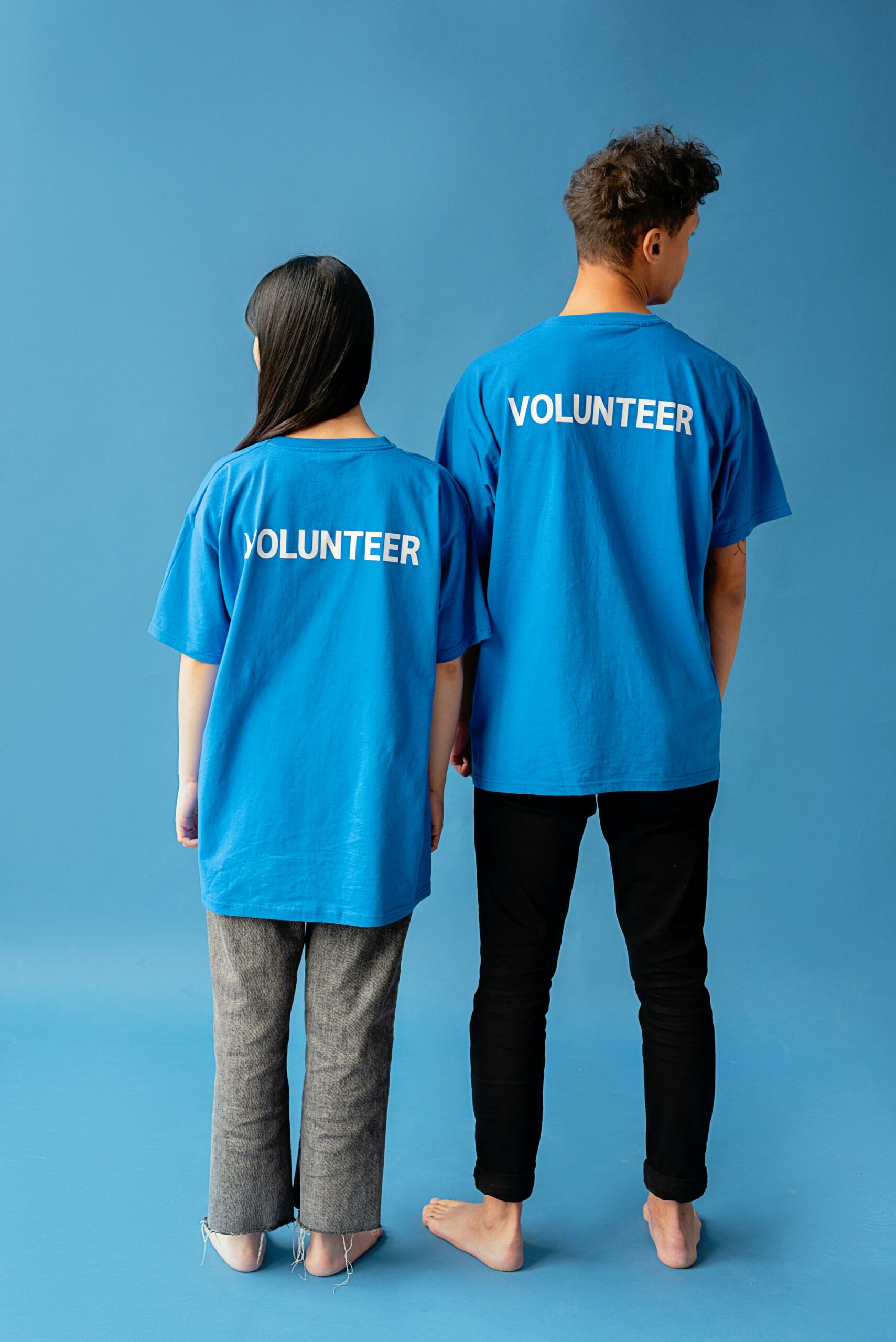 Back view of a man and woman wearing volunteer t-shirts, standing on a blue background.